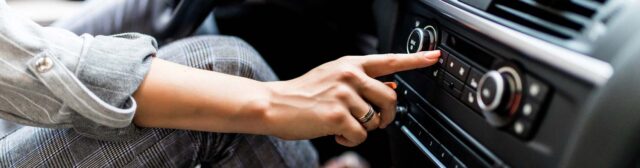 View of the dashboard in the interior of a car with the driver pressing a button on the center console.